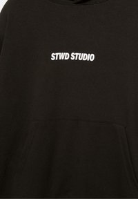 Sort hætte sweatshirt med hvid "STWD STUDIO" tekst trykt på brystet og en frontkangaroo lomme.