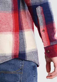 Rot-karierte Flanellhemd in Marineblau und Creme mit langen Ärmeln. Verfügt über Knopfmanschetten und einen abgerundeten Saum. Sichtbare Nähte und eine Denim-Tasche.