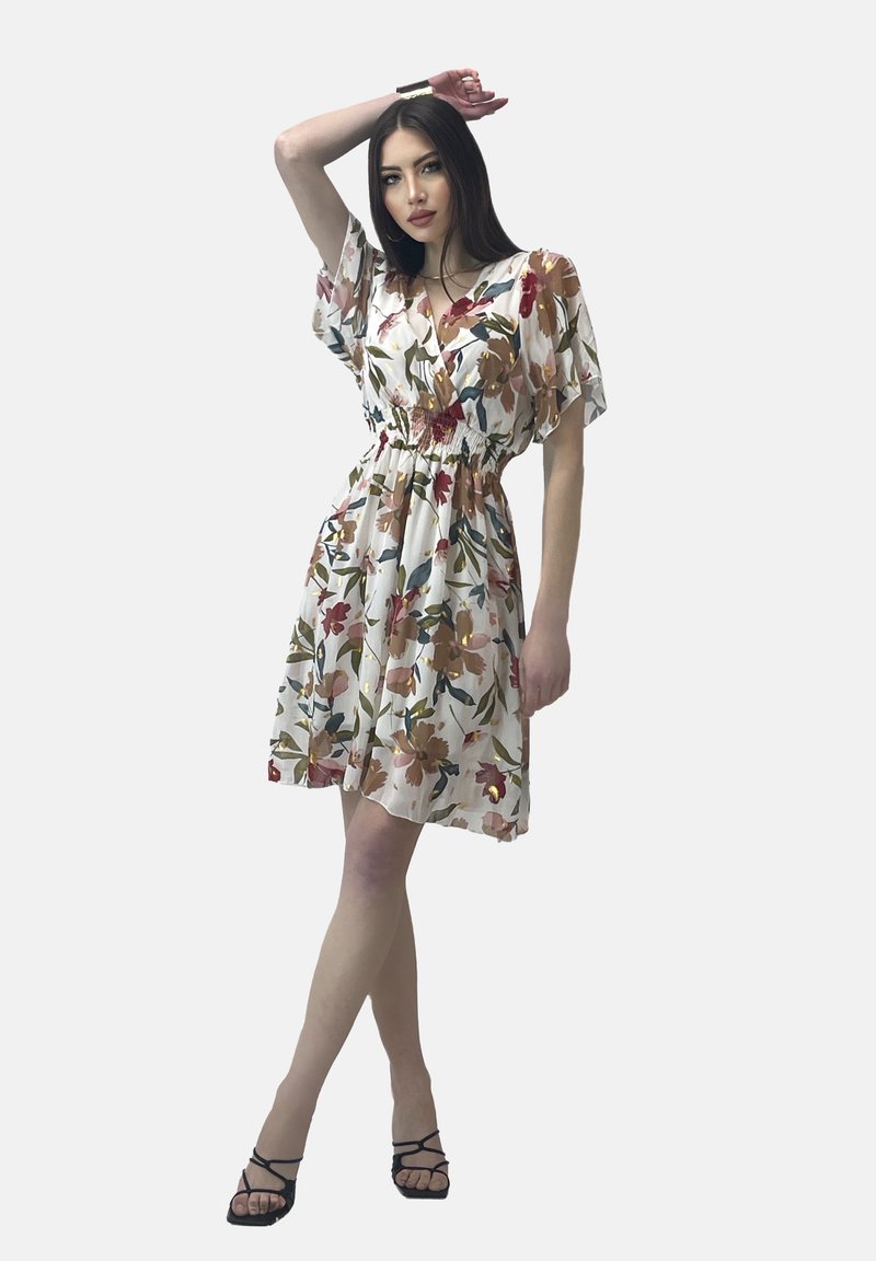 Bloemrijke jurk met korte mouwen, elastische tailleband, witte basis en multicolore bloemenpatronen. Vergezeld van zwarte sandalen met bandjes.