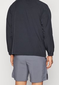 Zwarte, lange mouwen sportjack met elastische manchetten. Gecombineerd met grijze shorts met zijzakken en een iets losse pasvorm.