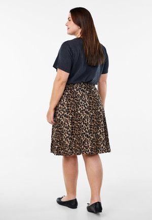 Suknja s leopard uzorkom, nabrana, izrađena od laganog materijala. Uparena s crnom majicom i ravnim crnim cipelama.