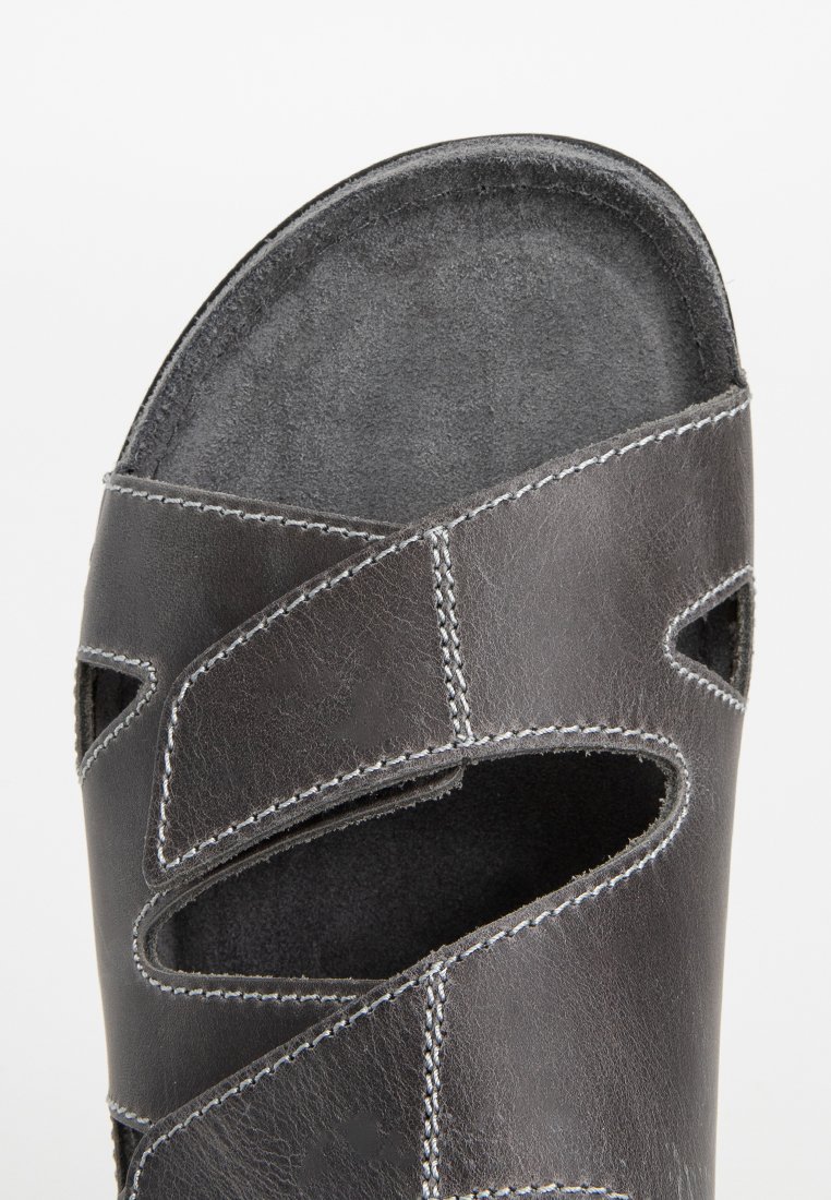 Sandale en cuir noir avec design découpé, surpiqûres blanches contrastantes et semelle intérieure en suédine texturée. Surface lisse et bords arrondis.