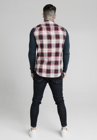 Koszula w kratę w czerwono-biało-szarym wzorze; długie granatowe rękawy; zestawiona z ciemnymi dżinsami i białymi tenisówkami.