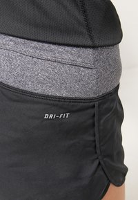 Pantalones cortos deportivos negros con una cinturilla gris; cuentan con la marca Dri-Fit. La tela es suave, con un ligero brillo y una textura de malla transpirable.