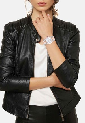 Sølv- og hvidt ur med en rund urskive, tre undermålere og et blødt pink rem. Båret på en persons håndled imod en sort læderjakke.