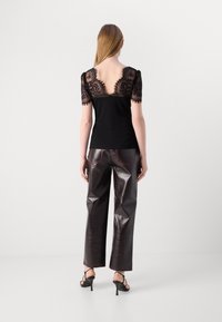 Haut noir avec des manches en dentelle et un dos décolleté, associé à un pantalon large brillant bourgogne et des sandales à talons noires.