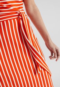 Czerwona i biała sukienka w paski z wiązanym detalem w talii. Gładka tekstura materiału, dopasowany krój i zwiewny dół.