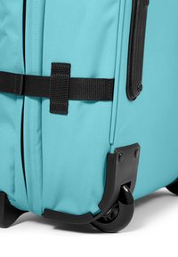 Türkisfarbener Rollkoffer mit Stoffaußenmaterial, schwarzen Gurten und robusten schwarzen Kunststoffrädern. Verfügt über verstärkte Ecken für hohe Strapazierfähigkeit.