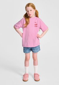 Rosa bomullströja med korta ärmar och körsbärstryck, i kombination med blå denimshorts och rosa sneakers med kardborrestängning.