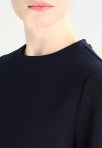 Navy sininen teksturoitu vaate, jossa on pyöreä pääntie ja näkyvät saumat, neutraalilla taustalla.