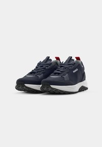 Paire de baskets Hugo bleu marine avec semelles blanches, semelles extérieures crantées noires, languettes rouges au talon et lacets noirs sur fond gris.