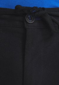 Czarne spodnie z zapięciem na guzik i regulowanym pasem ze ściągaczem, o gładkiej fakturze i subtelnych detalach przeszyć.