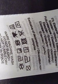 Oznaka za njegu odjeće, bijeli materijal s crnim ikonama. Upute za pranje, sušenje i peglanje odjevnog predmeta koji sadrži 5% elastana.