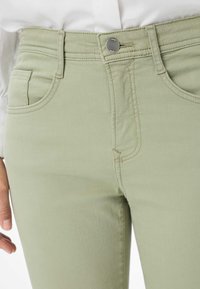 Grüne Baumwollmischungshosen mit glatter Textur, Fünf-Taschen-Design und subtilen Nähten. Verfügt über einen silbernen Knopfverschluss in der Taille.