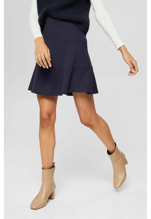 Laivastonsininen kellohame joustavasta kankaasta, jossa on istuva vyötärö ja kerroksellinen helma. Yhdistetty vaaleanbeigeihin nilkkureihin, joissa on paksu korko.