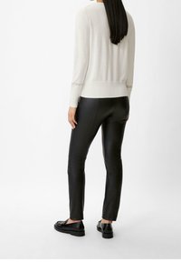 Jasnobeżowy sweter o dopasowanym kroju, zestawiony z czarnymi skórzanymi spodniami. Gładka faktura, długie rękawy, subtelne prążkowane akcenty przy mankietach i dolnym brzegu.