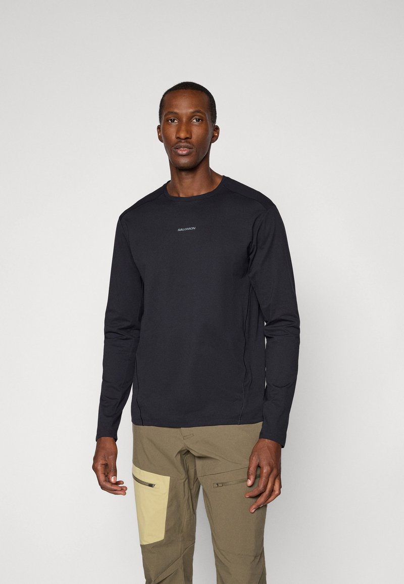Zwarte longsleeve t-shirt van gladde stof, met een ronde halslijn en een subtiele logo op de borst. Geen patronen of versieringen.