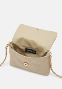 Borsa trapuntata beige con tracolla in oro e chiusura a bottone. L'interno presenta una fodera morbida con etichetta del marchio.