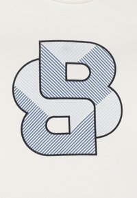 Bijela pamučna majica s velikim plavim grafičkim prikazom slova "B" s dijagonalnim prugama, oivičenim crnom bojom.