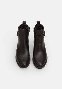 Botas de tobillo de cuero negro con un acabado suave, que presentan una suela plana, punta redondeada y detalle de hebilla ajustable en el tobillo.