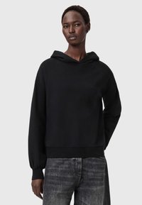 Felpa nera con vestibilità ampia, maniche lunghe e cappuccio con coulisse. Tessuto morbido, polsini e orlo a costine, abbinata a jeans grigi scoloriti.