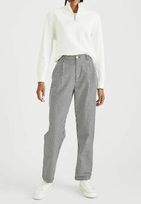 Felpa bianca con zip, pantaloni a vita alta a quadretti bianchi e neri con pieghe, abbinati a sneakers bianche per un look casual.
