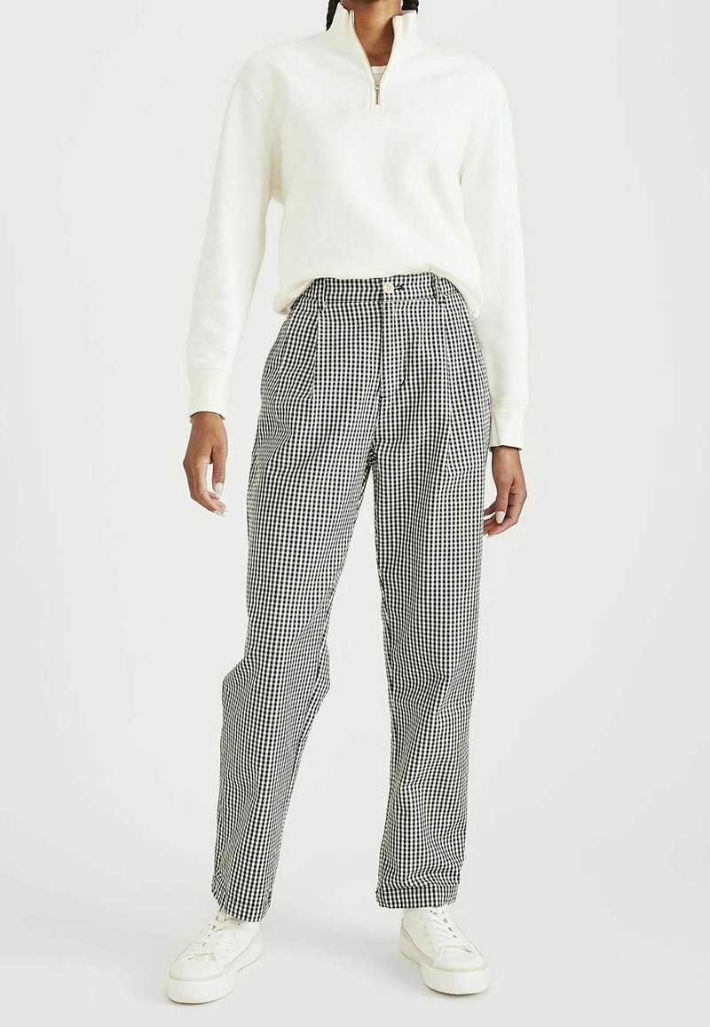Felpa bianca con zip, pantaloni a vita alta a quadretti bianchi e neri con pieghe, abbinati a sneakers bianche per un look casual.
