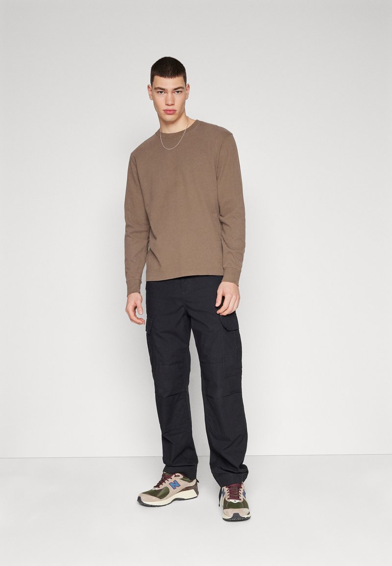 Braunes Langarmhemd, schwarze Cargo-Hose mit Seitentaschen und mehrfarbige Sneaker; minimalistisches Design vor einem neutralen Hintergrund.
