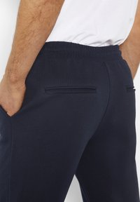 Marineblauwe sweatpants met een gestructureerde stof, elastische tailleband en twee platte achterzakken. Gladde oppervlakte met een getailleerd ontwerp.