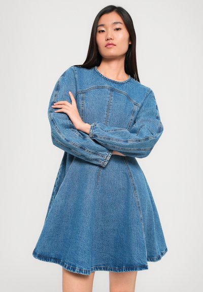 Džínsová šaty s dlhými, nafúknutými rukávmi, okrúhlym výstrihom a rozšírenou sukňou. Obsahuje viditeľné švy a mierne rozstrapkaný lem.