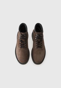 Brown suede ankle boots with black laces, featuring a padded collar and contrasting black rubber sole, designed for comfort and durability.