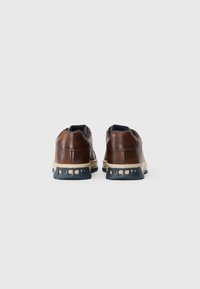 Pruunid nahast sneakers siniste aktsentidega, ümarate joontega, eksklusiivse tekstuuriga pind ja suur valge tald, millel on külgedel bränding.