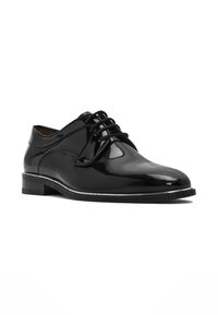 Zwarte gepatineerde leren oxford-schoen met een ronde neus, vetersluiting en een lage hak. Vaatbare textuur met minimale decoratieve accenten.