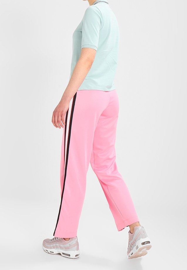 Personne marchant vêtue d'un haut à manches courtes bleu clair, de pantalons roses avec des rayures latérales noires et de chaussures de sport rose clair sur fond blanc.