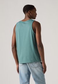 Groene mouwloze tanktop van zacht katoen, met een ronde halslijn en een relaxte pasvorm, gecombineerd met lichtblauwe verwassen spijkerbroek.
