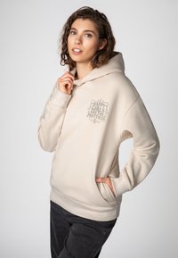 Lichtbeige hoodie met een ontspannen pasvorm, voorzien van een geprinte tekst in grijs: "HAPPY GIRLS ARE THE PRETTIEST." Zacht stof, kangoeroezak.