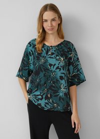 Blouse florale teal à manches courtes, avec un décolleté en forme de clé et une coupe ample. Présente de grands motifs de fleurs noires et crèmes sur un tissu texturé.