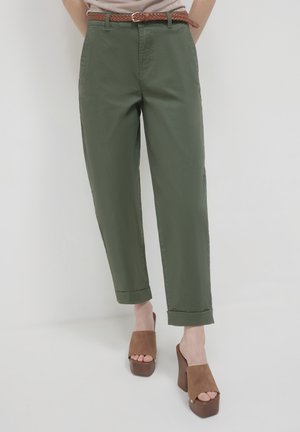Olivgrüne Hosen mit geradem Schnitt, umgeschlagenen Säumen und Gürtelschlaufen, kombiniert mit braunen Wildleder-Plateausandalen. Glatte Stofftextur.