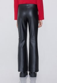 Černé kalhoty s rozšířenými nohavicemi z umělé kůže s hladkou texturou, vysokým pasem a čistými švy. Navrženy pro těsný střih.