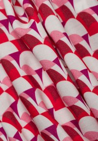 Tessuto colorato con un motivo geometrico di forme interconnesse rosse, rosa e viola su uno sfondo bianco, con una finitura liscia.