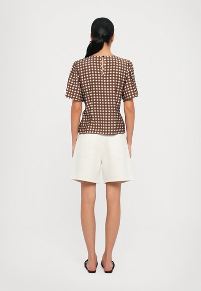 Top corto de manga corta de cuadros marrones con un corte recto y un escote en forma de lágrima en la parte posterior, combinado con pantalones cortos blancos hasta la rodilla. El material parece ligero.