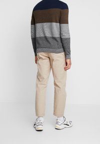 Neulepuserossa on tummansinisiä, ruskeita ja harmaita vaakaraitoja; se on yhdistetty beigenvärisiin housuihin ja valkoisiin lenkkareihin, joissa on harmaita ja keltaisia yksityiskohtia.