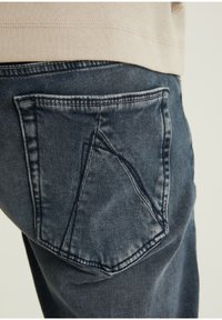 Mörka denimjeans har en unikt formad bakficka med en vinklad design. Tyget har en mjuk textur med subtila blekningsdetaljer.