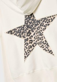 Krämfärgad hoodie med en stor stjärndesign i leopardmönster. Mjuk bomullsmaterial med ribbad ärm och fåll.