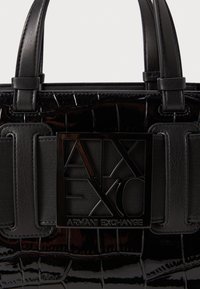 Borsa nera in pelle lucida, con un motivo testurizzato che ricorda la pelle di coccodrillo, caratterizzata da una prominente placca con logo nera e doppi manici.