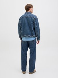 Denim švarkas ir kelnės vidutinio mėlynumo, su klasikiniu pjūviu, matomomis siūlėmis ir laisvu siluetu. Neutralios spalvos avalynė užbaigia įvaizdį.