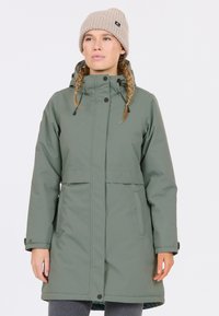 Grön isolerad jacka med hög krage och framfickor. Har en dragkedjestängning, justerbar dragsko i huva och en texturerad beige stickad mössa.