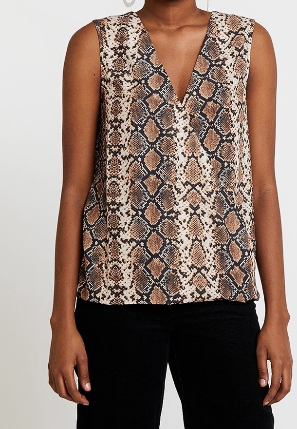 Top sans manches à encolure en V avec un motif serpent marron et noir, porté avec un pantalon noir, montrant le haut du corps et les bras.