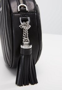 Angolo di una borsa in pelle nera con catena argentata e frange in pelle nera attaccate vicino alla cerniera.