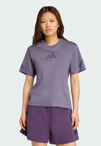 Lila tränings-T-shirt med kort ärm, slätt tyg, rund halsringning, med en mörkare lila logotyp på framsidan och matchande lila shorts.
